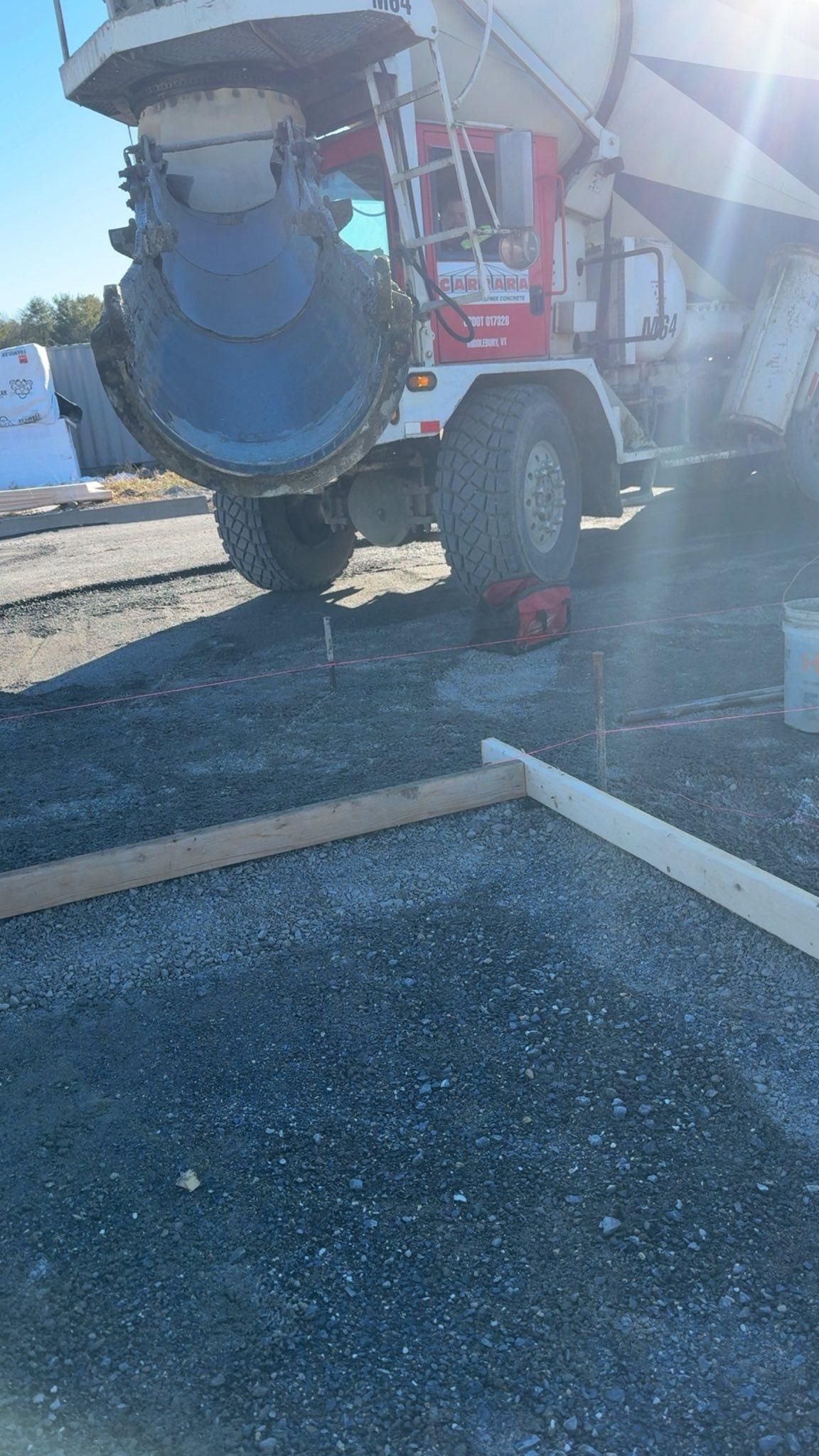 Red cement mixer truck on gravel near a white curb in bright sunlight