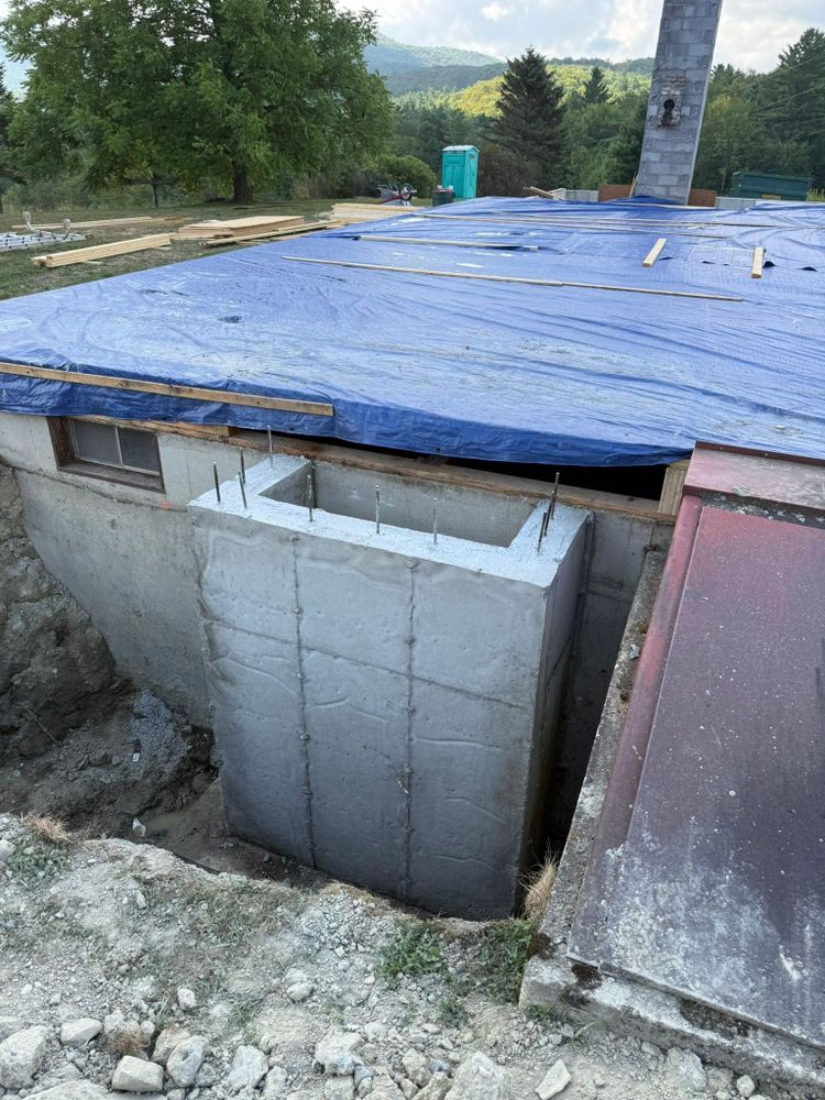 Partially built concrete structure with a blue tarp roof on a rocky hillside outdoors