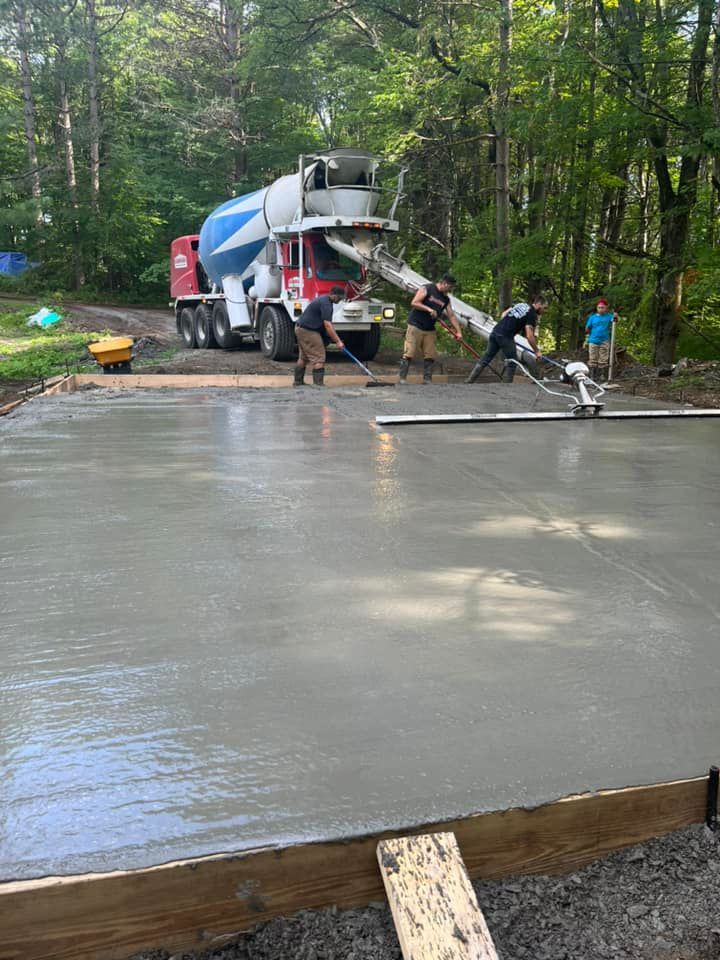 Workers pouring a concrete slab from a mixer truck in a wooded construction site