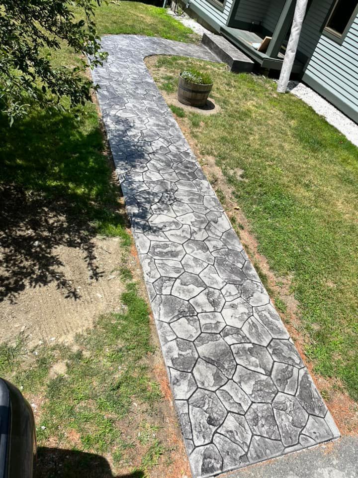 Stone garden walkway beside grass and house siding, with a small potted plant at the bend.