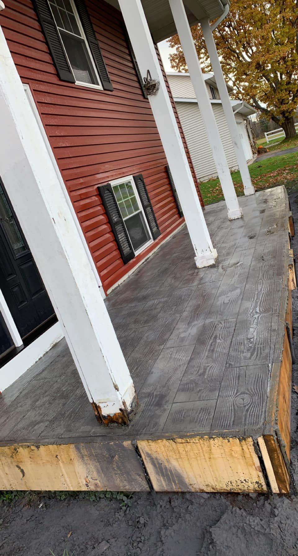 Wooden porch with white columns beside a red house, showing weathered floorboards and trim.