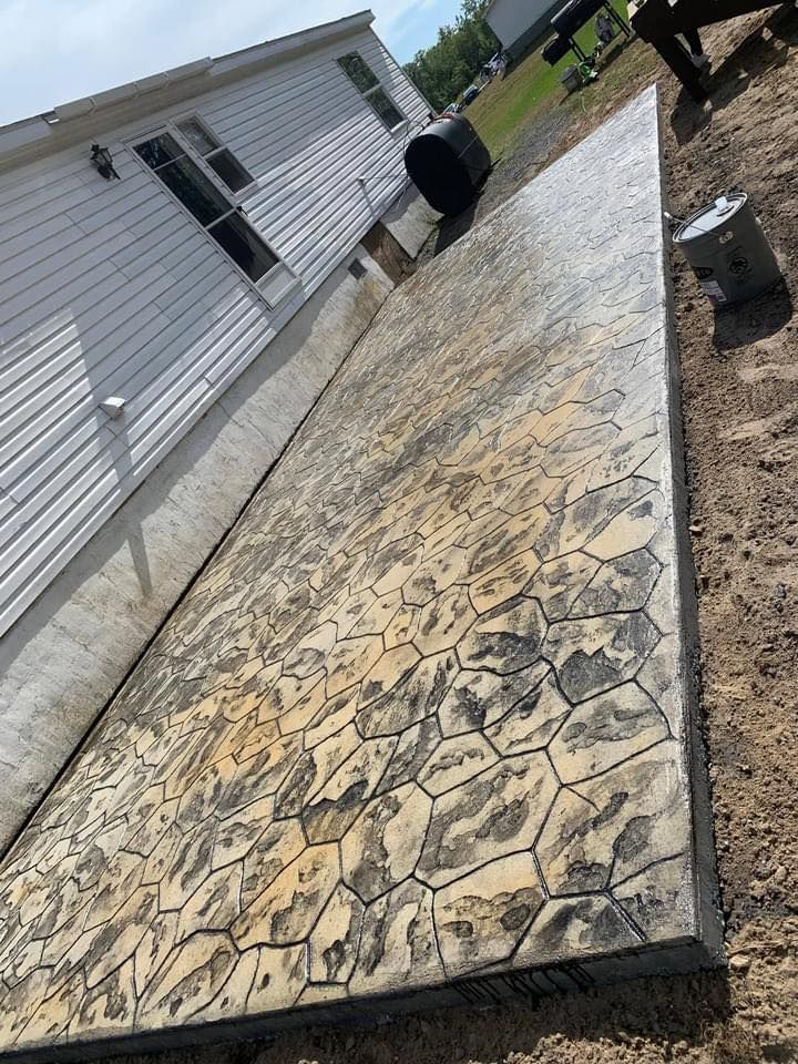 Stamped concrete patio beside a white house, with a black planter and newly landscaped dirt edges.