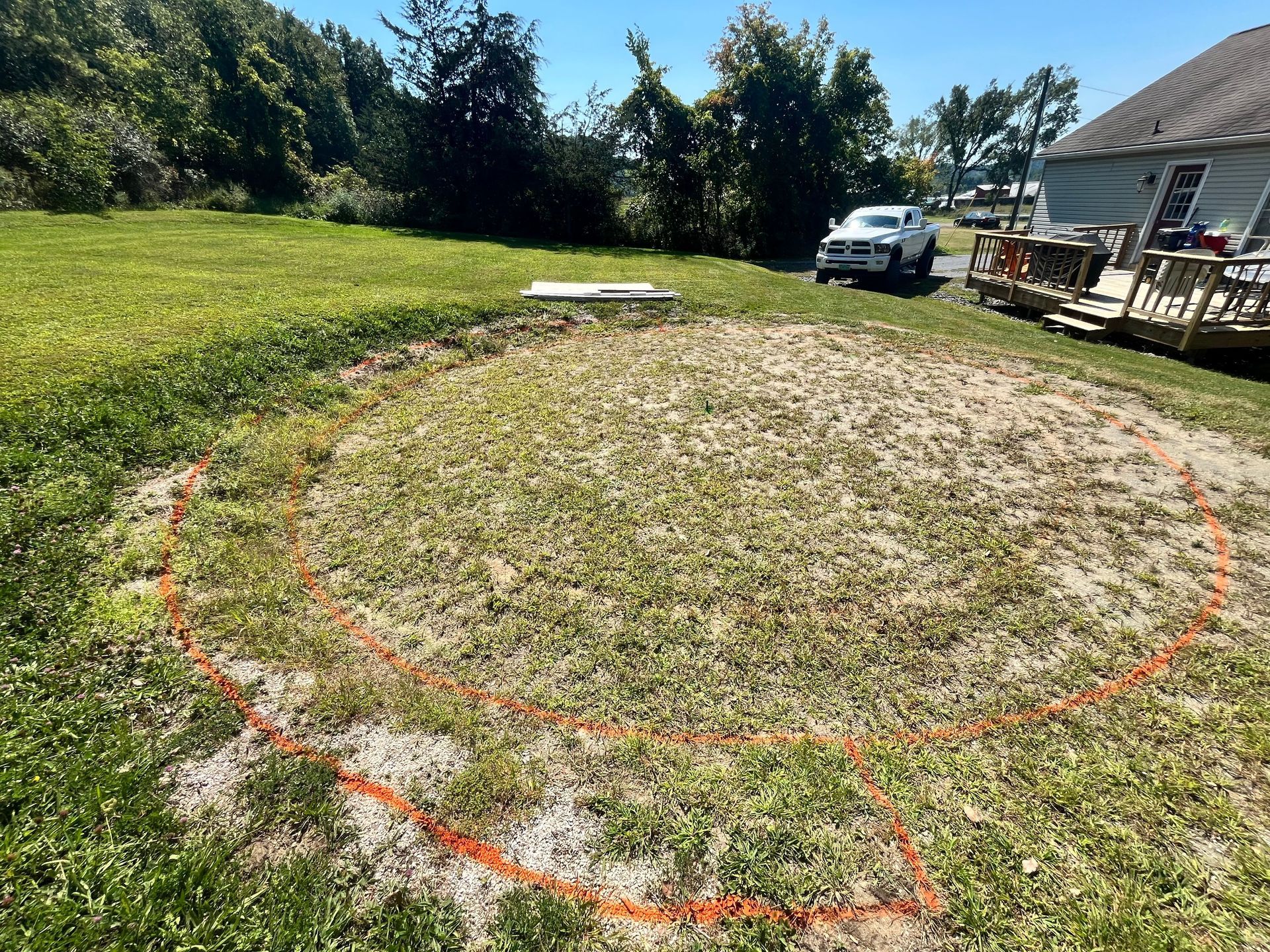 Orange-marked circular area in a grassy yard beside a house, with a white truck in the background.