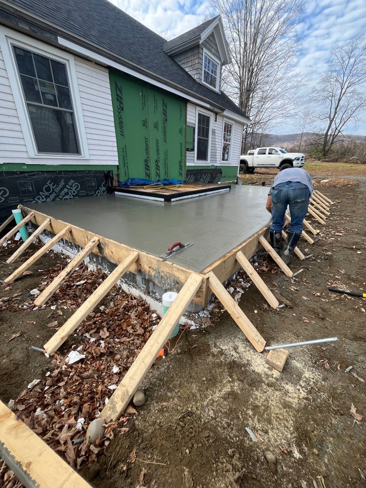 Worker smoothing concrete patio beside house with wooden forms and green siding