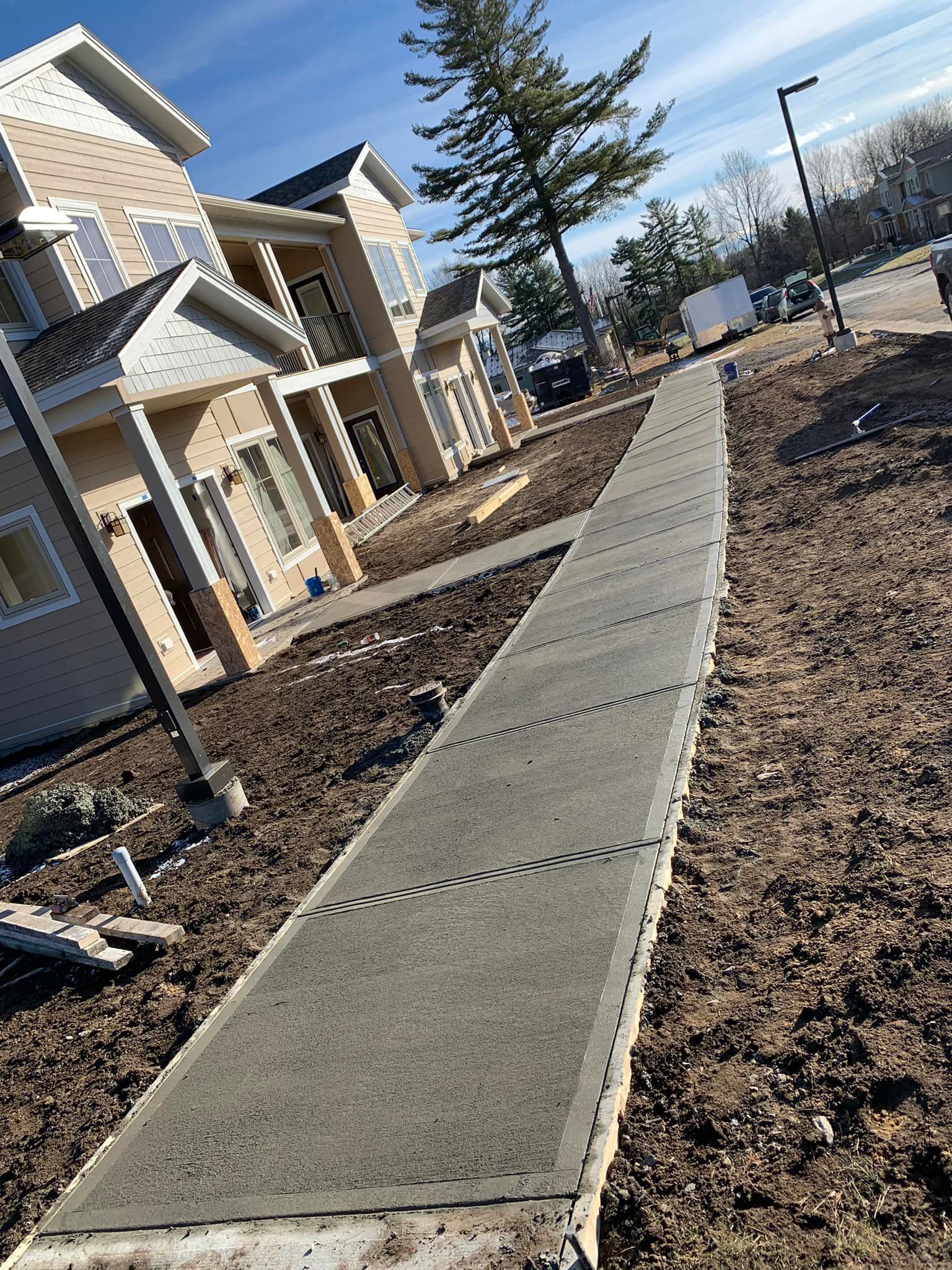 Concrete sidewalk beside new townhouses in a residential construction area.