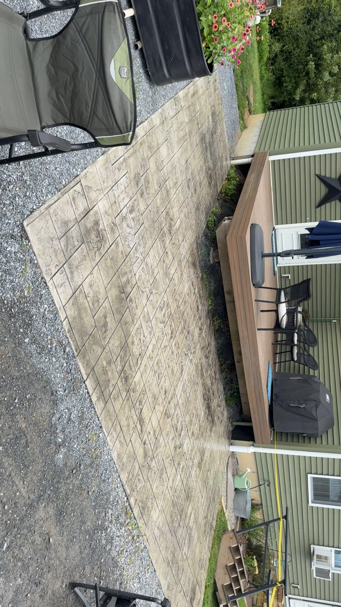 Gravel backyard with a wooden deck, patio chairs, and a grill beside a house and garden beds.