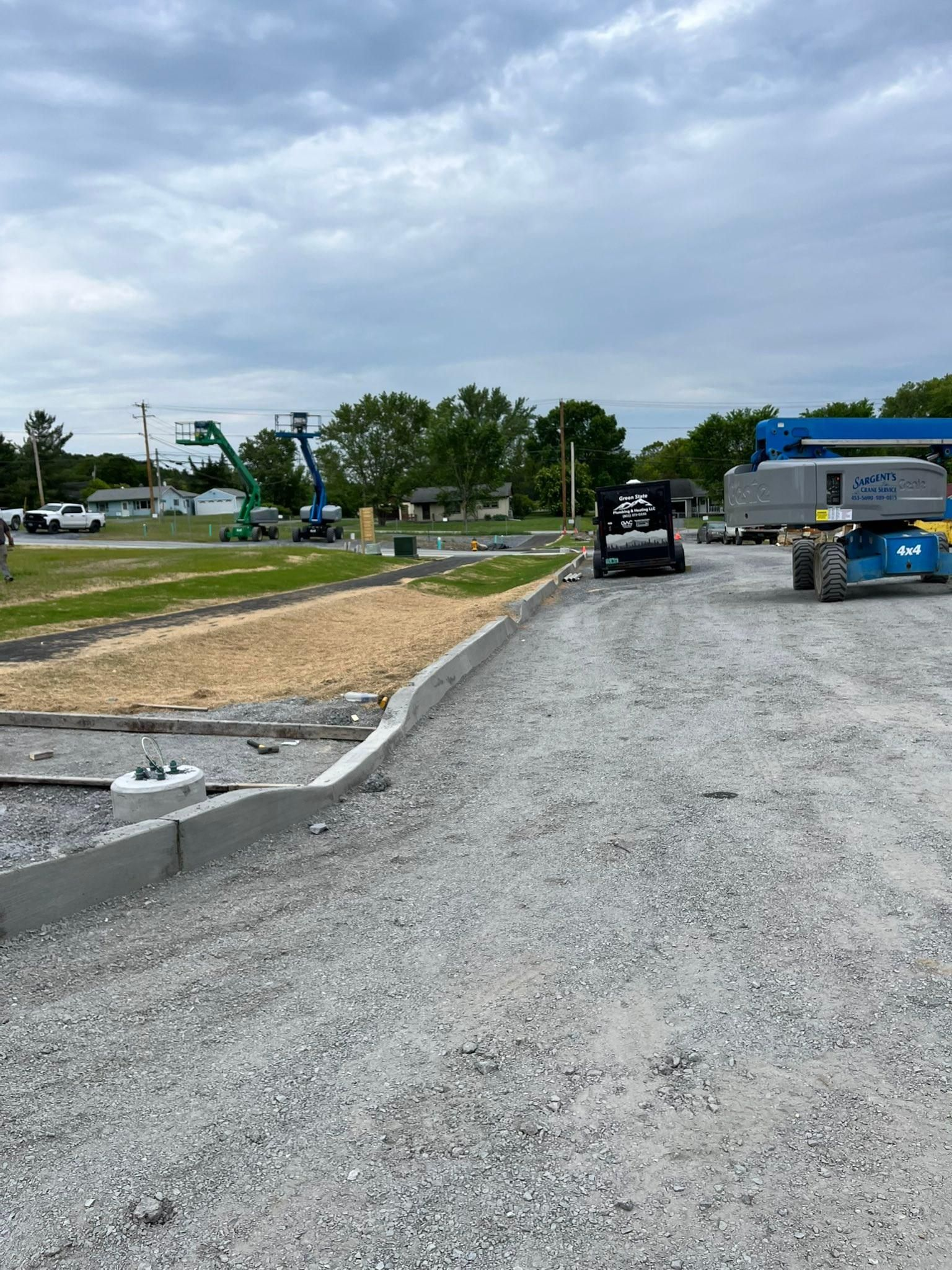 Gravel parking area with a black truck, blue dumpster, and cloudy sky beside a road