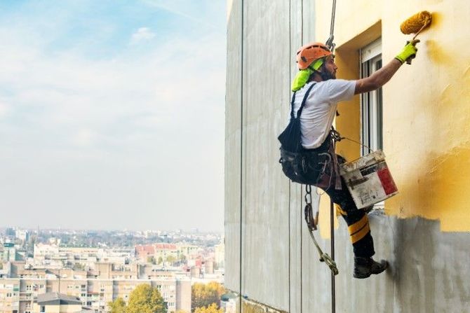 Window washer rappelling down a high-rise, cleaning a building exterior with a city view below