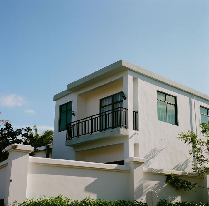 Modern white two-story house with balcony and large windows under a clear blue sky