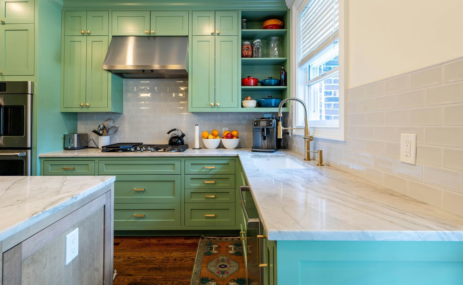 Mint-green kitchen with stainless range hood, white countertops, and bright window light