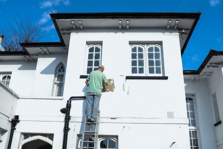 Worker on a ladder painting the exterior of a white house under a blue sky