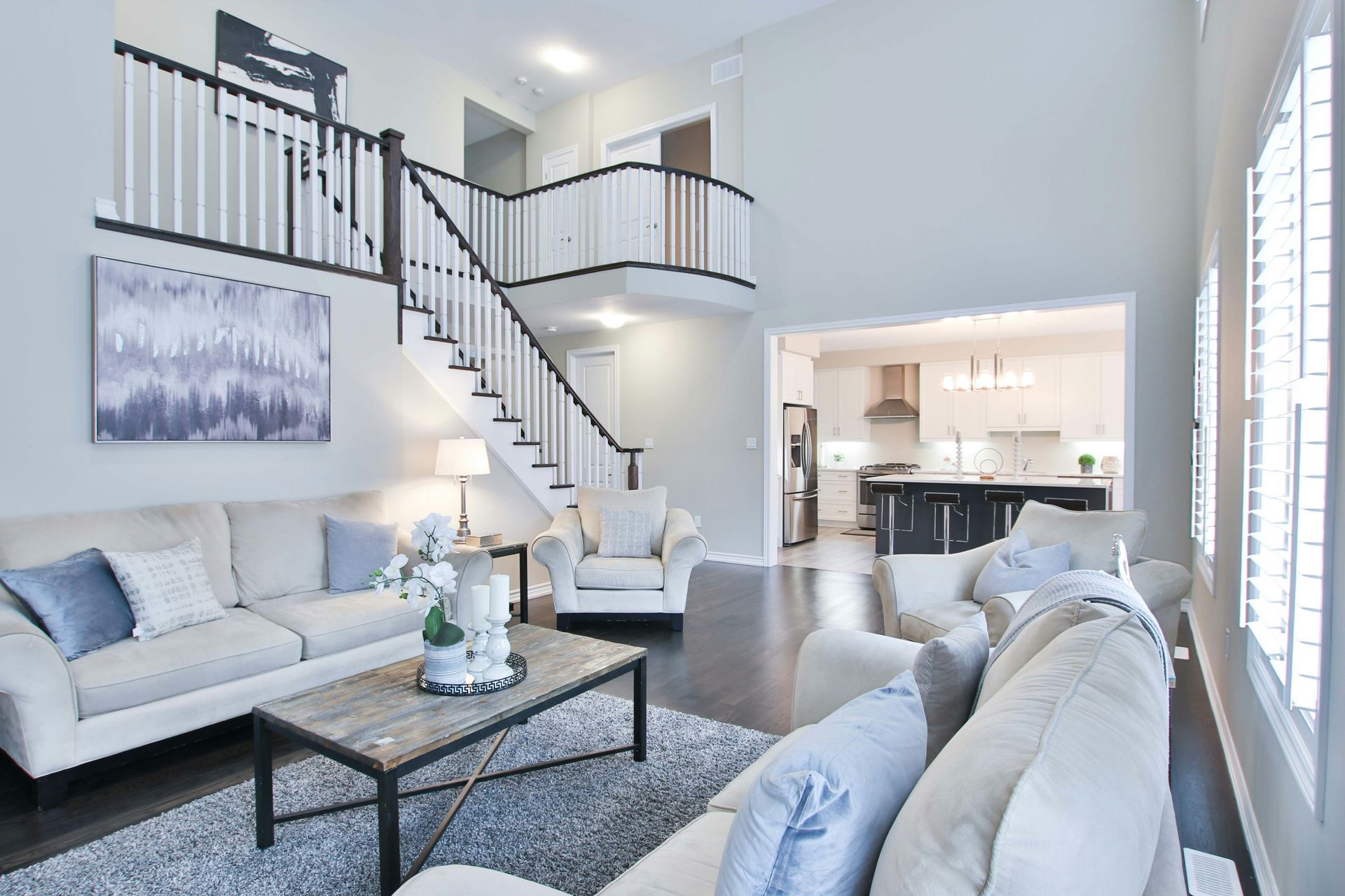 Bright modern living room with white sofas, staircase, and open kitchen in the background
