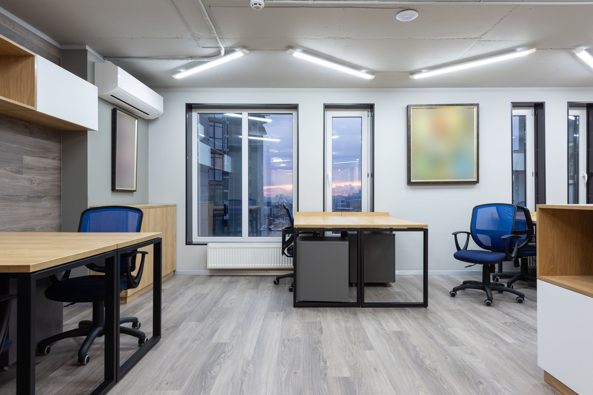 Modern office room with desks, blue chairs, large windows, and city view