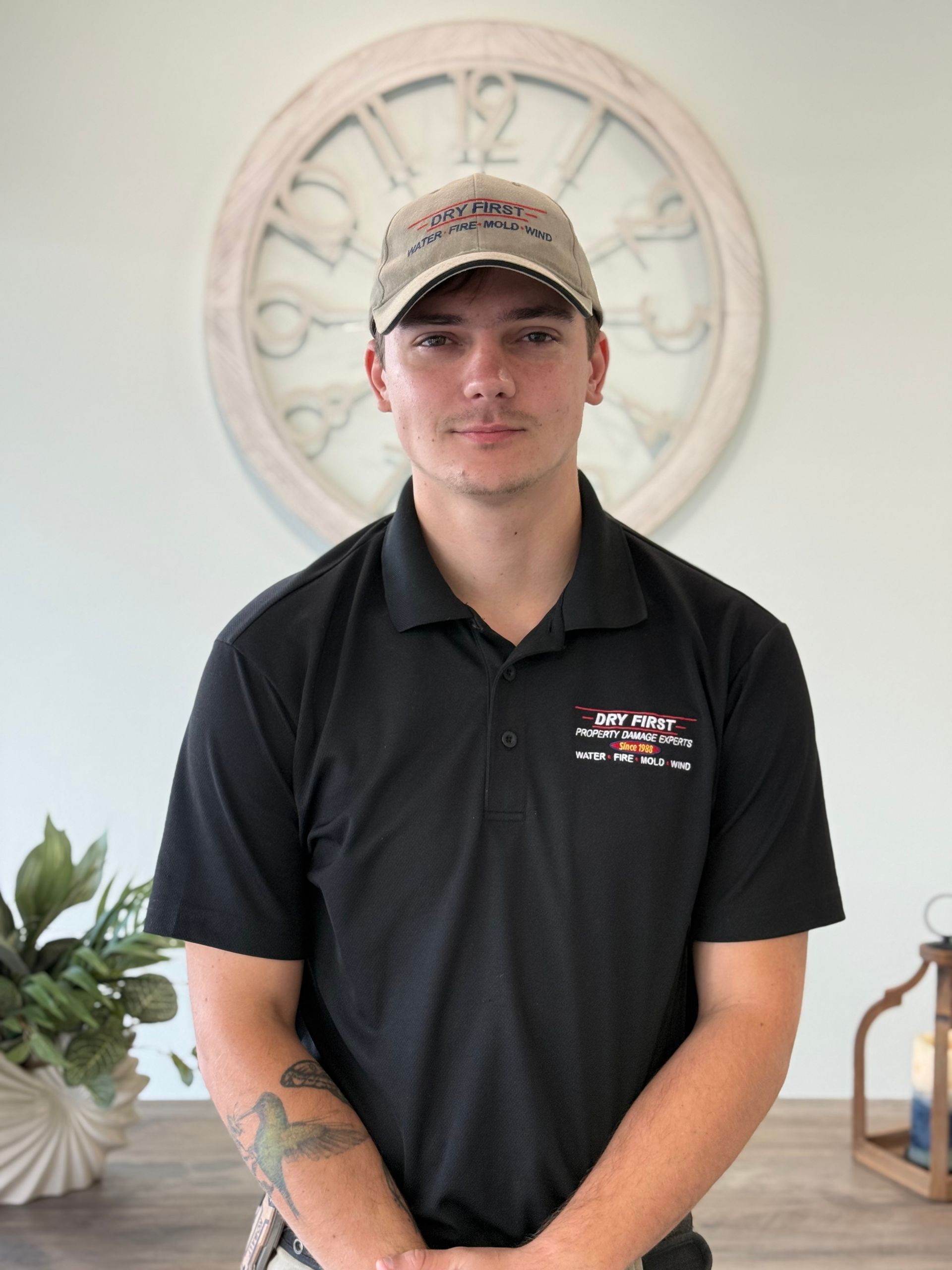 A team member of dryfirst restoration company in a black polo shirt and baseball cap stands centered 