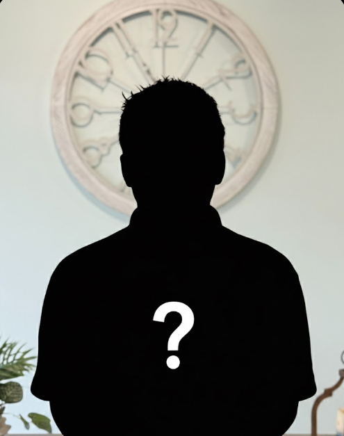 A silhouette of a person standing against a wall with a large clock in the background.