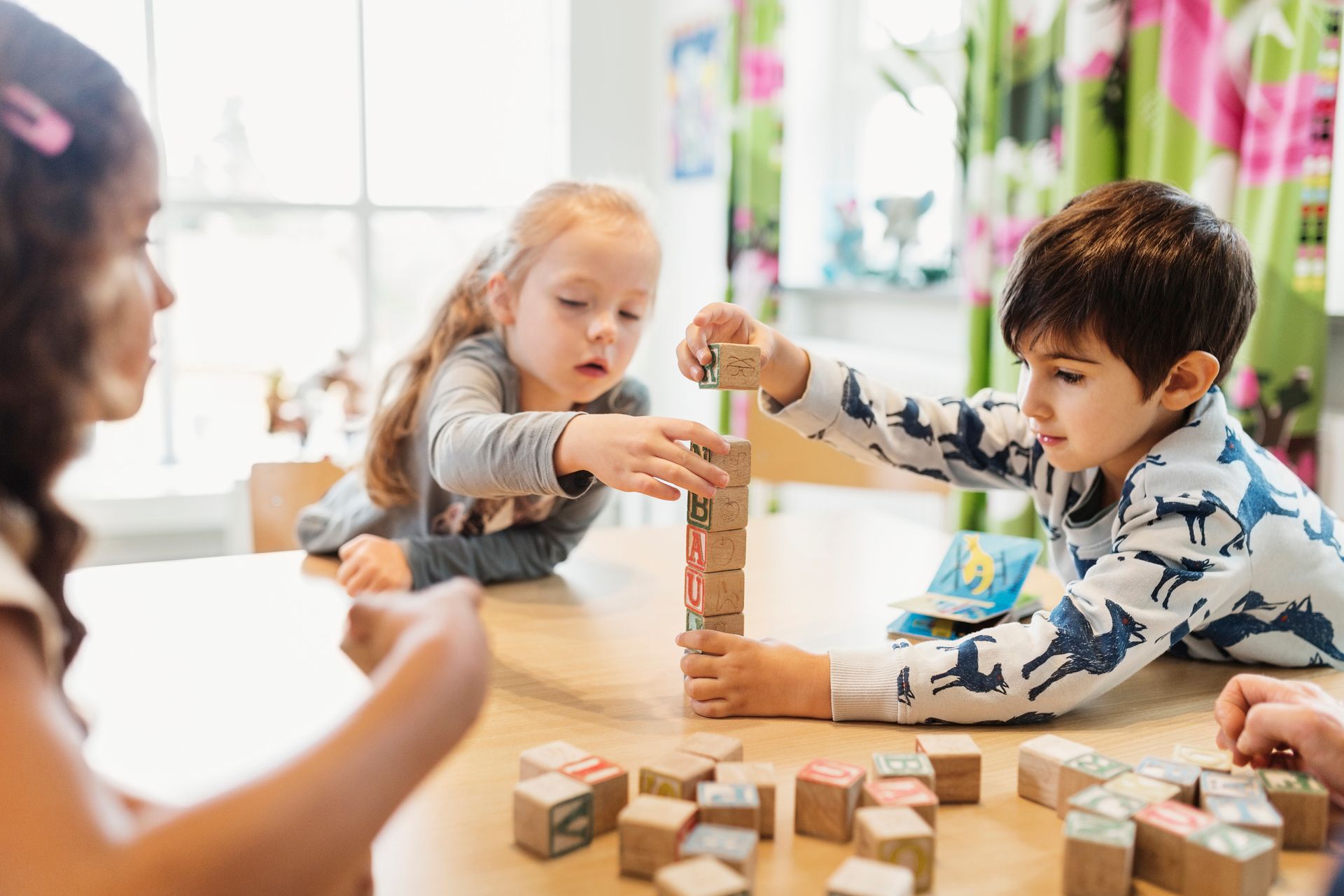 Un gruppo di bambini sta giocando con dei blocchi di legno seduti a un tavolo.