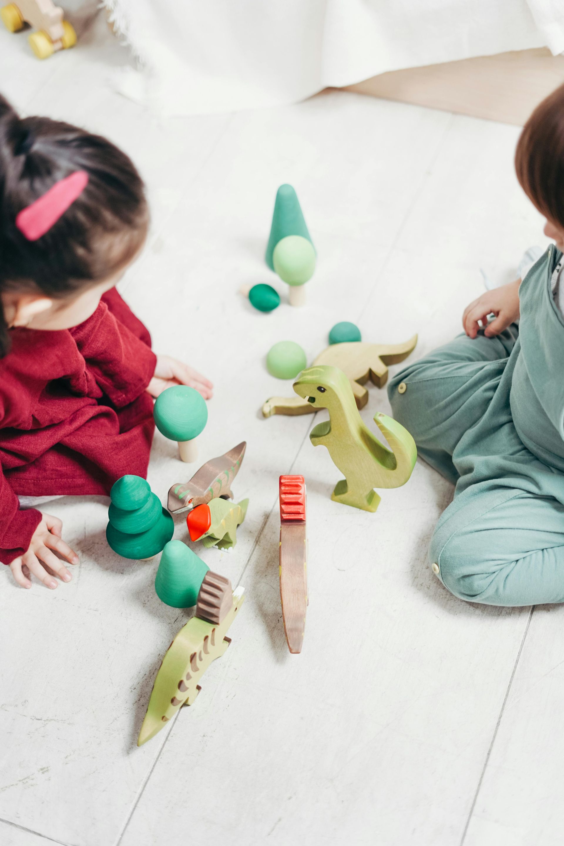 Un bambino e una bambina sono seduti sul pavimento e giocano con dei giocattoli di legno.