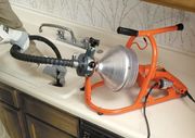 Clogged sink drain being cleared with an orange plumbing auger and a wet vacuum hose