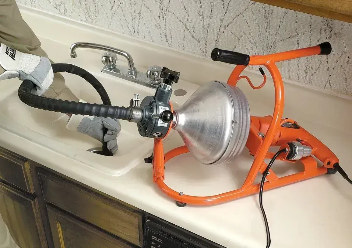 Clogged sink drain being cleared with an orange plumbing auger and a wet vacuum hose