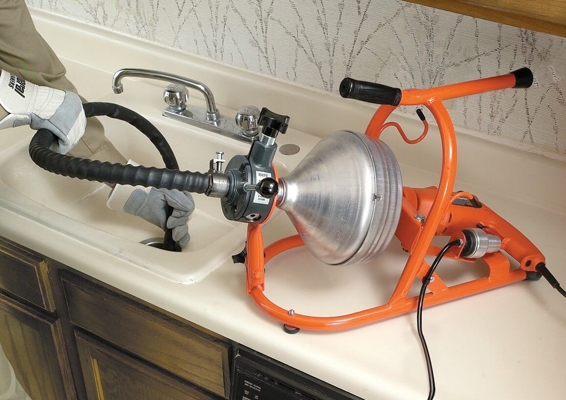 Clogged sink drain being cleared with an orange plumbing auger and a wet vacuum hose