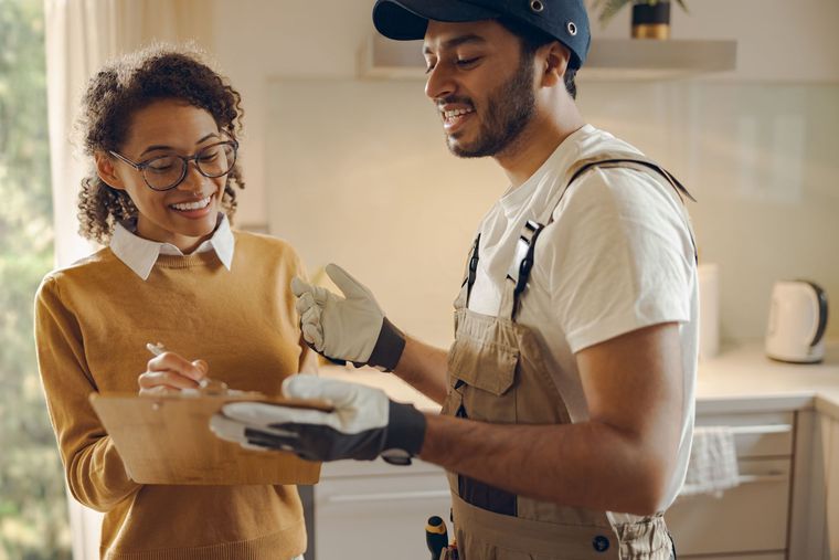 Two workers talking in a bright kitchen during a home renovation, one holding a drink.