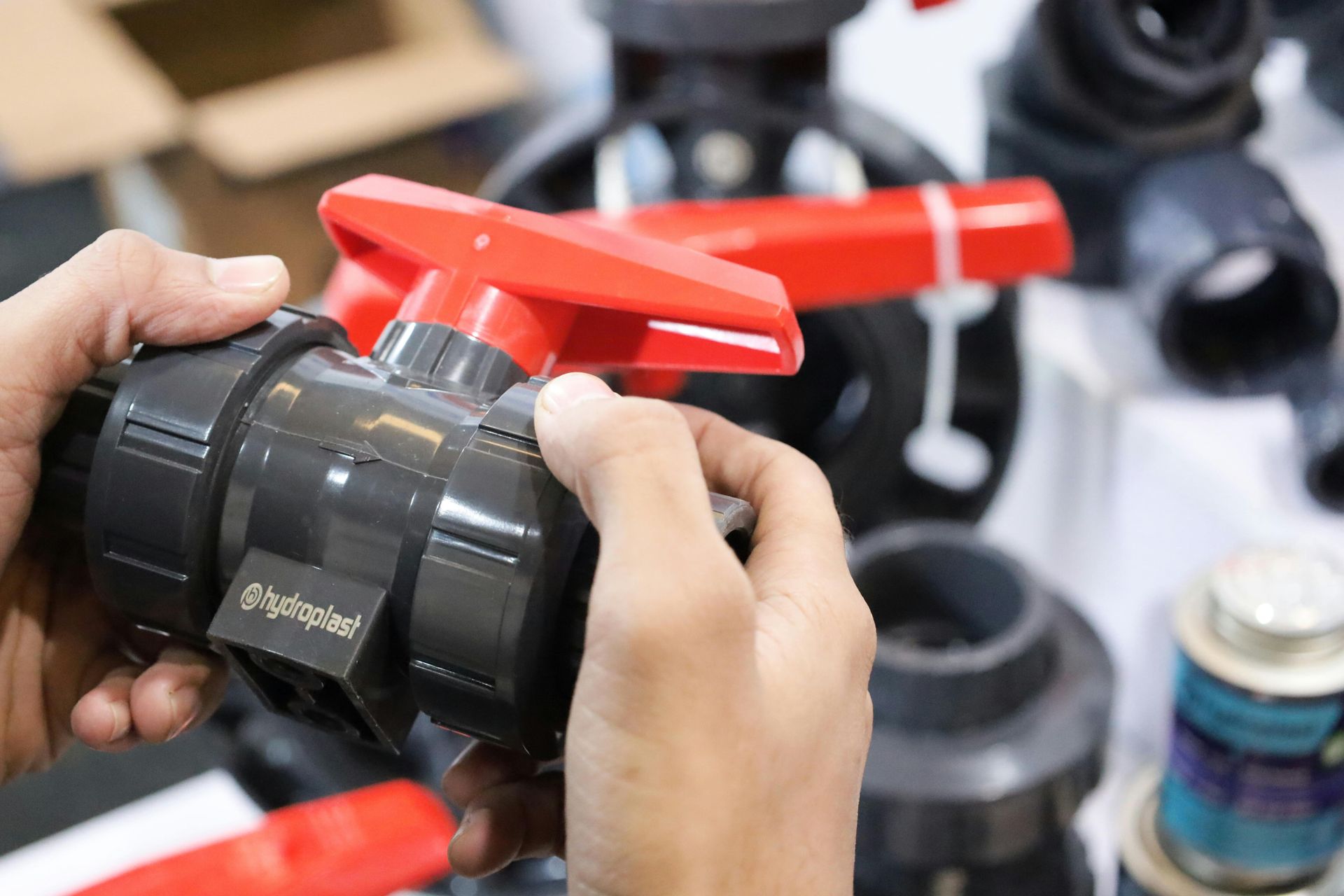 Hands adjusting a red valve on a black pipe fitting in a workshop setting