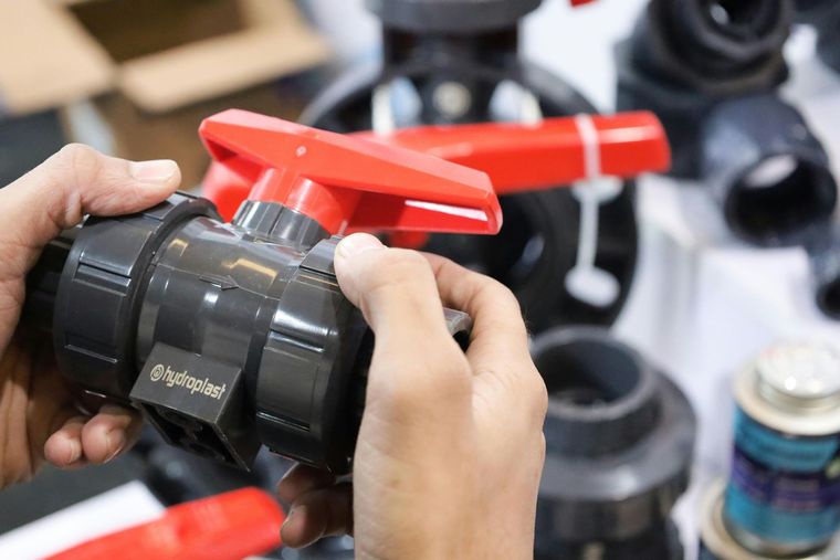 Hands adjusting a black pipe fitting with a red handle in a workshop setting