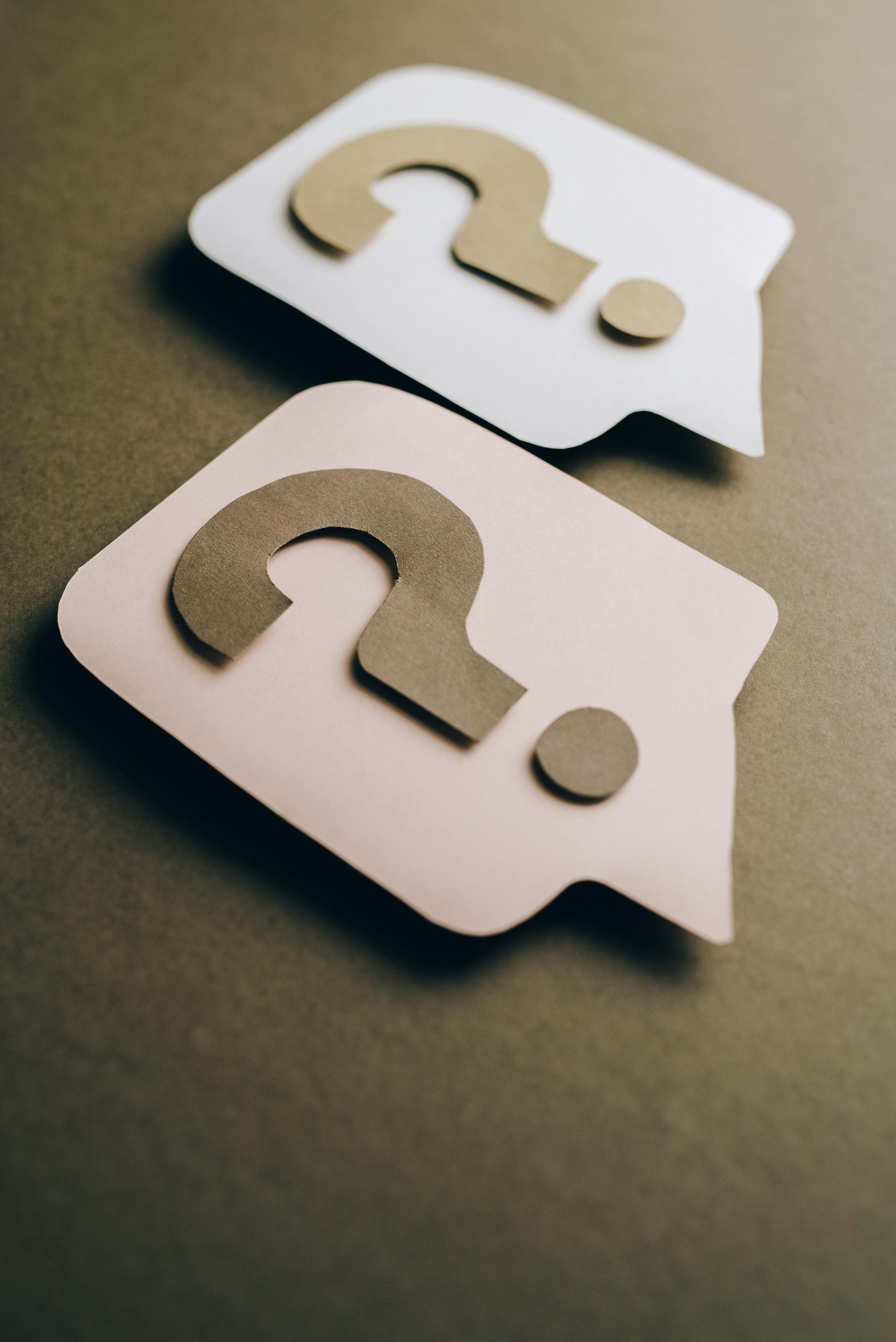 Two white speech-bubble icons with question marks on a gray surface