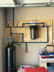 Two people inspect plumbing under a sink with tools in a white kitchen cabinet