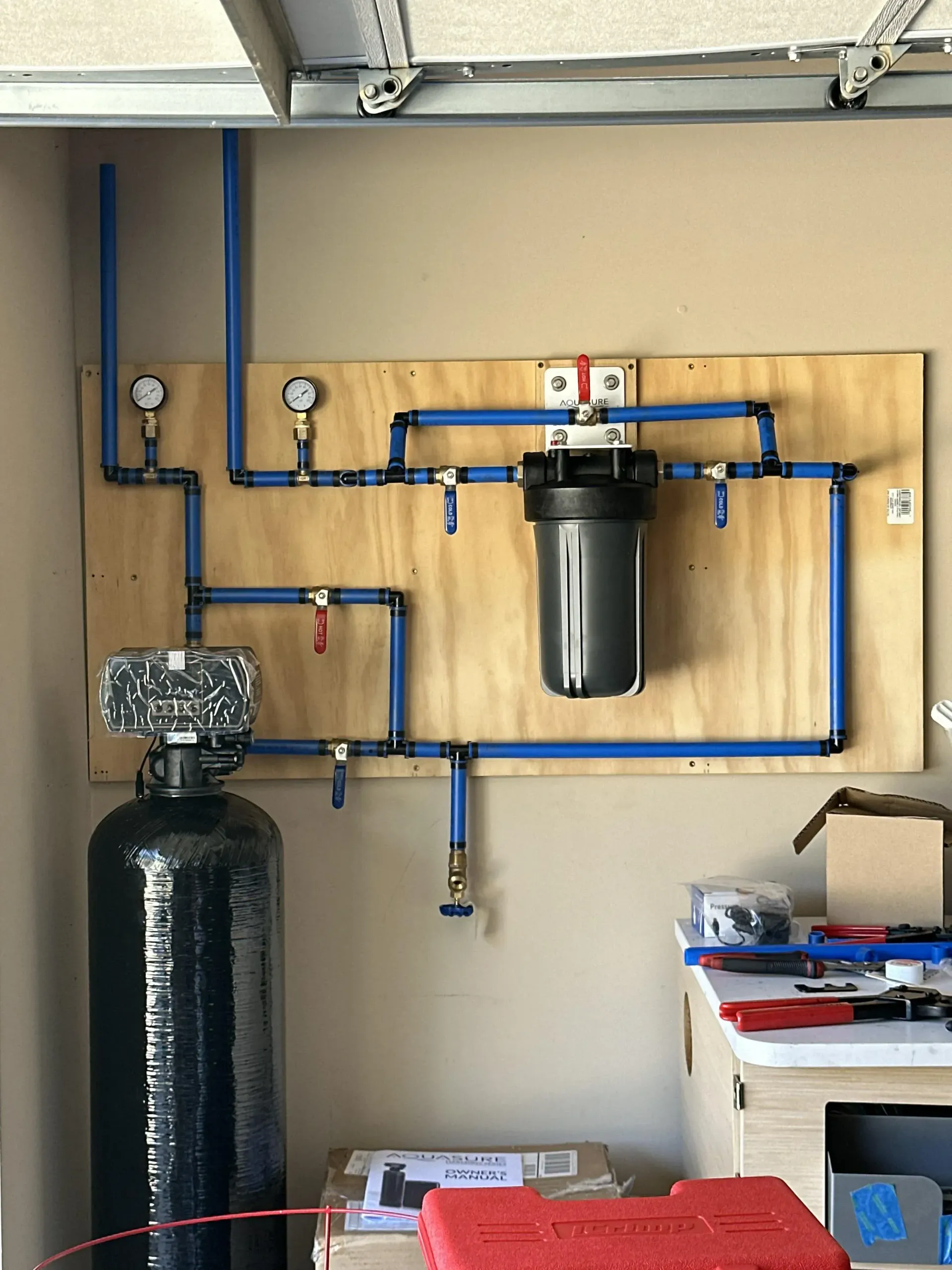 Two people inspect plumbing under a sink with tools in a white kitchen cabinet