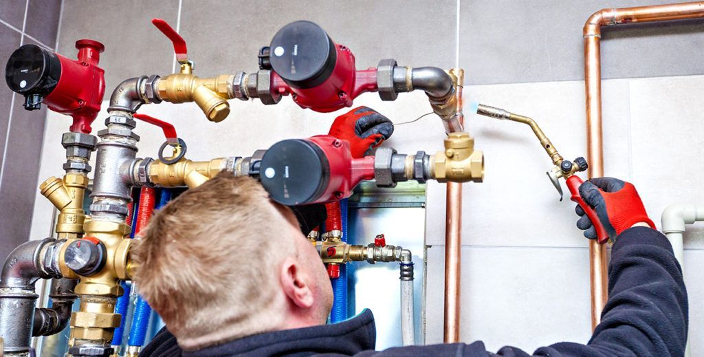 Plumber working on red and brass pipes and valves in a tiled utility room