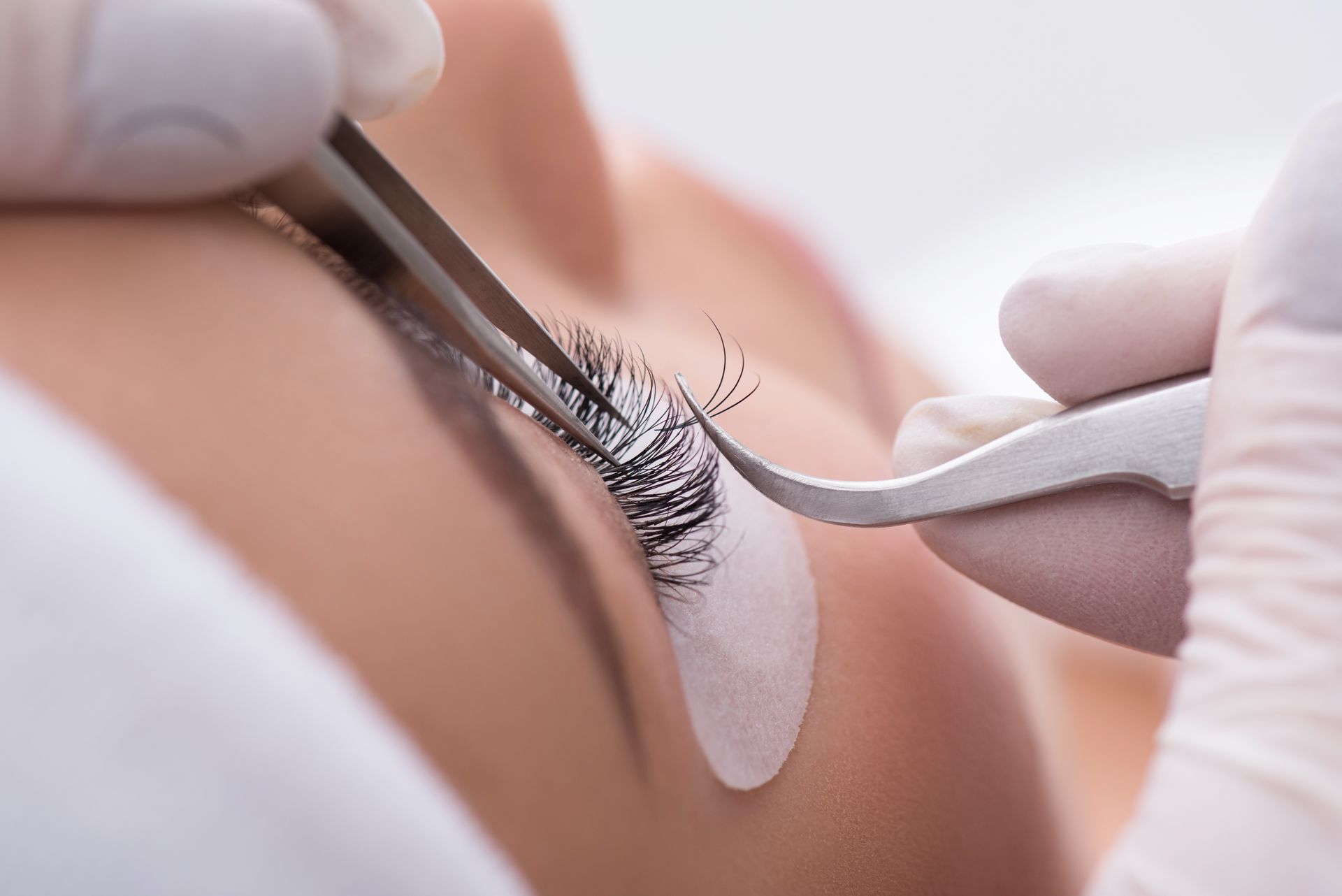 Close-up of a person applying eyelash extensions with tweezers to a woman's closed eye