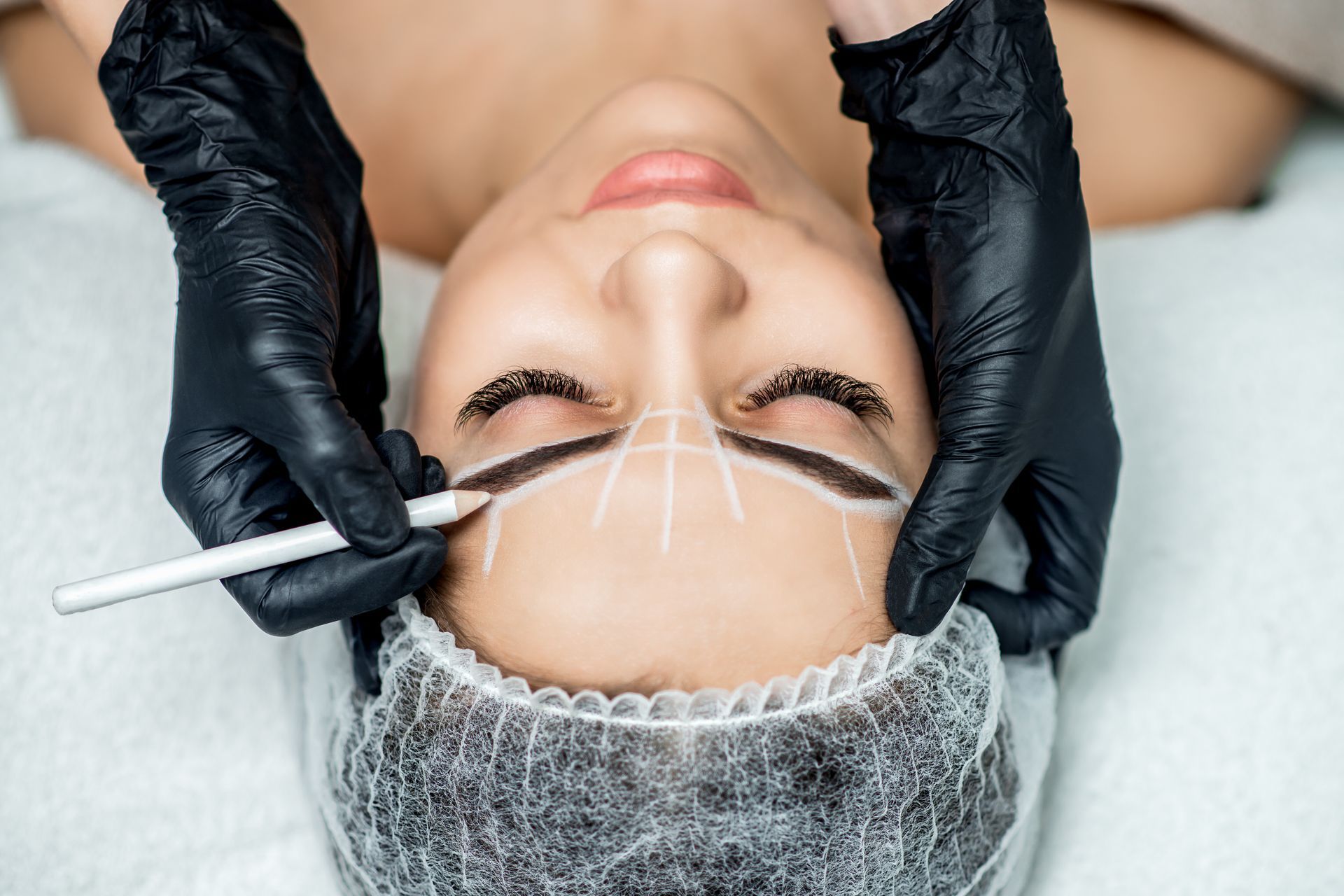 Cosmetician applying eyebrow treatment to a woman lying with eyes closed, close-up spa scene