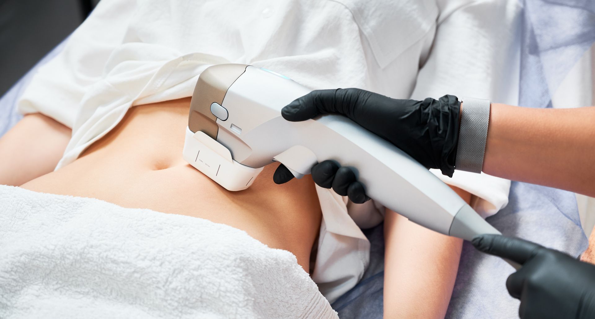 A medical professional uses a handheld device on a patient’s abdomen during a treatment procedure.