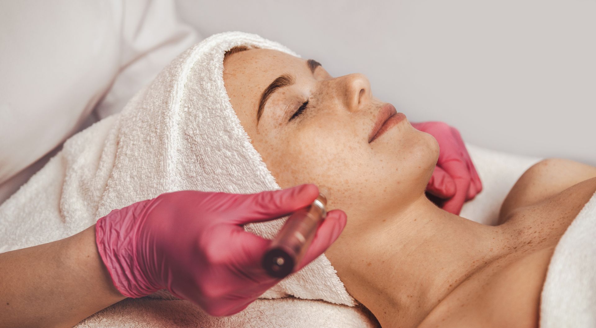 Facial spa treatment with a woman lying down, pink-gloved hands applying a roller along her jawline