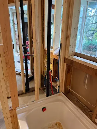 Unfinished bathroom framed with exposed studs, toilet flange, and windows visible.
