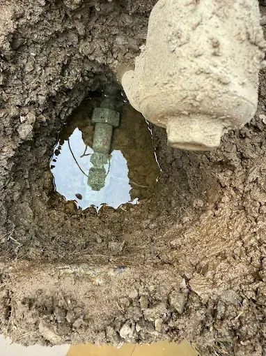 Dirt-lined hole with a pipe fitting and a white valve or cap at the top right