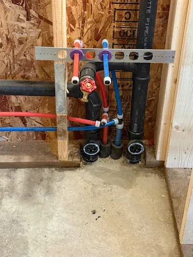 Plumbing rough-in with colored PEX pipes and drain lines in an unfinished wall framing.