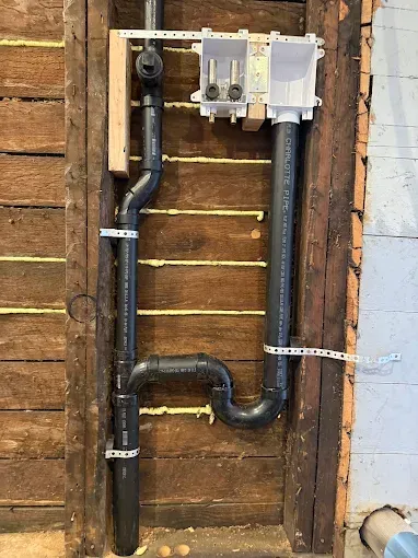 Black pipes and electrical boxes mounted on unfinished wood framing inside a wall.
