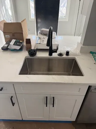 Kitchen sink with black faucet, white countertop, and cabinets under a window.