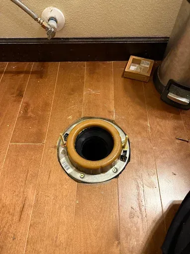 Open floor access hole in a wooden floor near a wall and baseboard