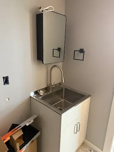 Small utility sink and wall-mounted cabinet in a beige room, with exposed wiring and unfinished walls.