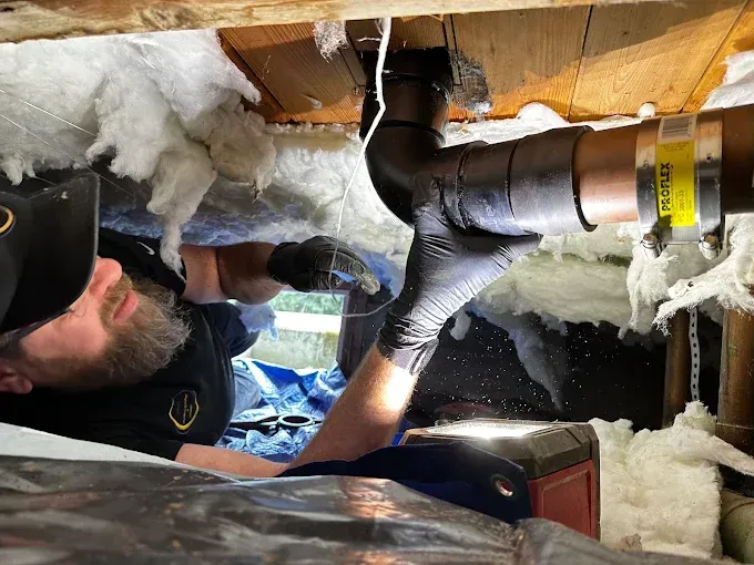 Worker installing ducting in an attic with exposed insulation and wood framing