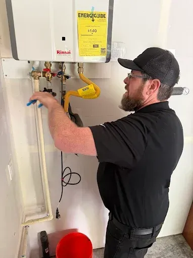 Technician adjusting pipes beneath a wall-mounted water heater in a utility room.