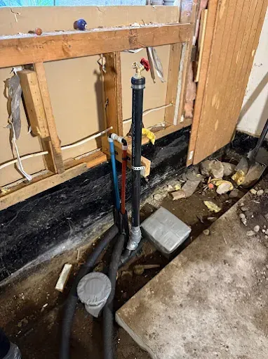 Exposed plumbing and open wall cavity beside a concrete floor during home renovation