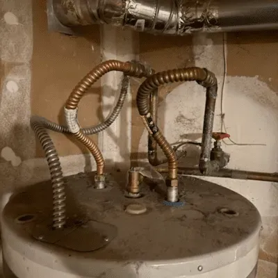 Corroded water heater top with several flexible pipes and fittings in a utility closet