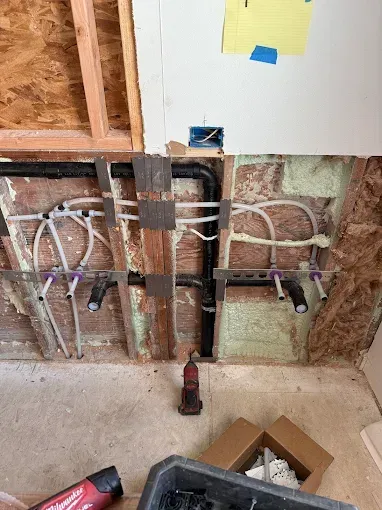 Exposed bathroom wall plumbing with pipes and green insulation during renovation