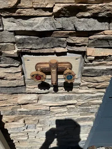 Outdoor stone wall with a brass hose bib and two decorative faucet handles, one red and one blue.