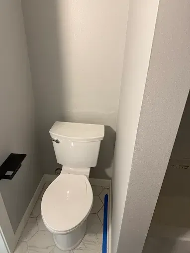 Small white toilet in a narrow bathroom alcove with a black wall-mounted toilet paper holder.