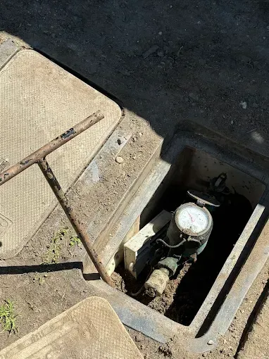 Open utility meter box in pavement with exposed water valve and black interior